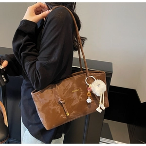 Close-up of deep brown glossy leather tote bag featuring a plush charm and shoulder straps