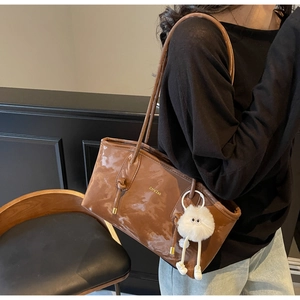 Detail of glossy brown leather tote bag with gold logo and white plush charm