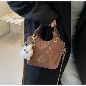 Detail der glänzenden braunen Beuteltasche mit Plüsch-Anhänger und Handgriff