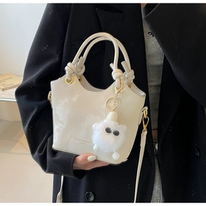 Detailansicht der weißen Handtasche mit Knotengriff, Goldbeschlägen und Plüsch-Anhänger