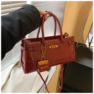 Detail of dark red glossy leather handbag with gold twist lock and mini bag charm