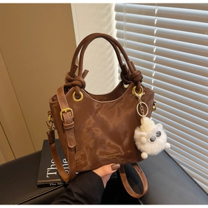 Detail einer braunen Vintage-Beuteltasche mit goldenen Beschlägen und Schaf-Plüschanhänger