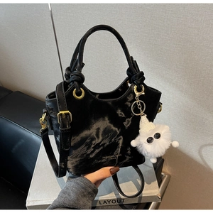 Detail der schwarzen glänzenden Beuteltasche mit Goldbeschlägen und Plüschanhänger