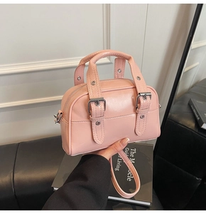 Détail d'un mini sac à main rose avec ceintures décoratives et boucles en métal argenté