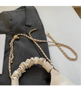 Close-up of beige pleated handle bag with gold metal chain and spherical adjuster