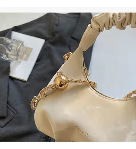 Close-up of beige ruched cloud bag featuring gold spherical clasp and chain strap