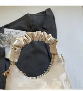 Close-up of beige crescent bag featuring pleated cloud handle and gold chain detail