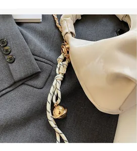 Detail of cream pleated cloud bag featuring gold chain and woven rope with metallic orb