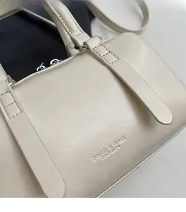 Gros plan du sac Boston en cuir crème montrant le grain naturel et le logo embossé