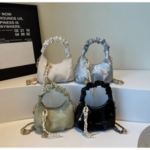 Array of pleated dumpling bags in cream, silver, green, and black on a white tiered display