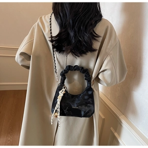Detail of black glossy cloud bag featuring gold branding and chic woven chain strap
