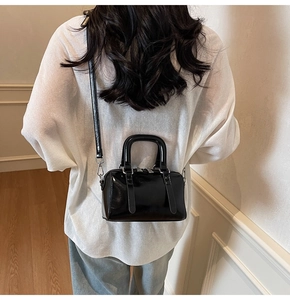 Détail d'un mini sac Boston noir brillant porté en bandoulière par un mannequin de dos