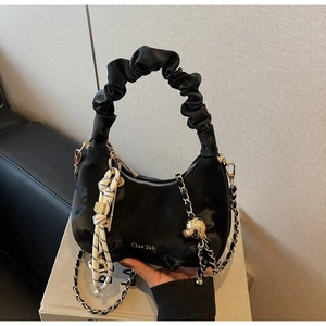 Detail of black pleated cloud bag featuring a gold ball charm and woven chain strap