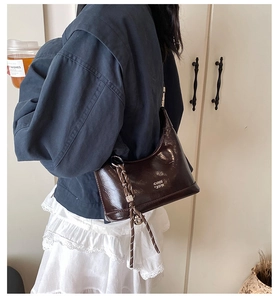 Side view of a dark brown hobo bag with white text and braided rope detail on a model