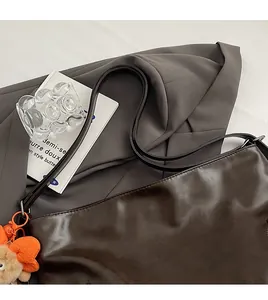 Close-up of deep brown leather shoulder bag featuring a bright orange plush butterfly charm