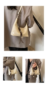 Detail of cream patent leather baguette bag featuring braided cord and silver bell charm