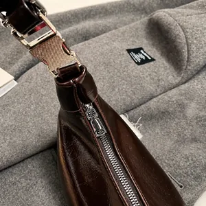 Detail view of silver metal zipper and hardware on deep brown glossy leather handbag