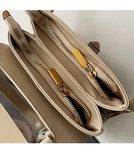 Detail of dual zipper compartments and golden hardware on the beige crossbody bag