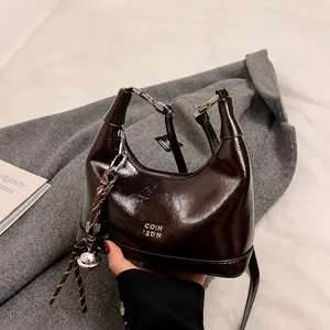 Detail of dark brown glossy leather handbag with silver hardware and braided bell charm