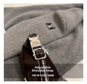 Detail of adjustable shoulder strap with silver metal buckle on a dark brown glossy bag