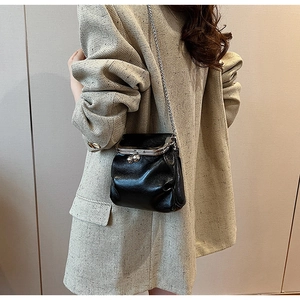 Primo piano di una borsa a tracolla in pelle lucida nera con catena su un blazer grigio