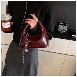 Detail of burgundy patent leather crescent bag with woven strap and metal orb charm