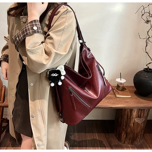 Detail of burgundy leather tote bag with monster charm on model in cafe setting