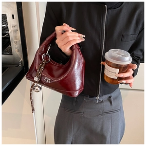 Detail of burgundy patent leather hobo bag with silver bell charm and woven rope
