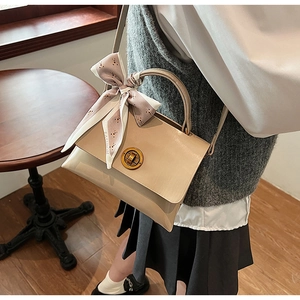 Detail of cream crossbody bag featuring a golden twist lock and a fashion silk scarf