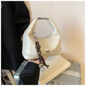 Detail of a creamy white patent leather hobo bag with unique metal buckle handle and charms