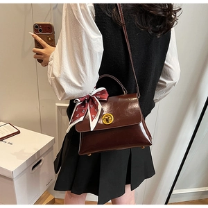 Classic brown messenger bag with silk scarf on handle worn as a crossbody purse