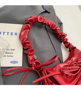 Close-up of bright red pleated handbag with glossy finish and ribbon bow detail