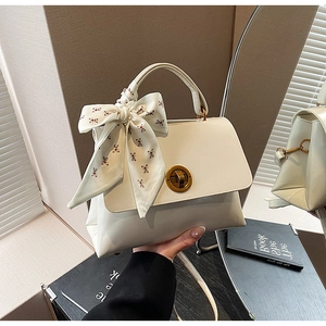 Detail of white leather shoulder bag featuring a gold round twist lock and a cute bear scarf