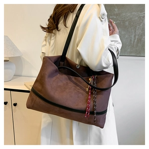 Détail du sac cabas en daim marron avec bandoulières en cuir noir et pendentif doré
