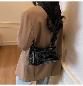 Detail of black patent leather shoulder bag featuring bow decor and ruched strap on model