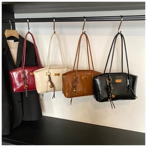 Detail of four glossy faux leather shoulder bags in red, beige, brown, and black with charms
