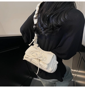 Detail of white glossy leather shoulder bag featuring a pleated strap and bow design