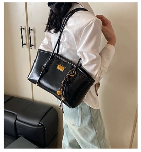 Detail of black PU leather shoulder bag with gold metal plaque and woven ball charm