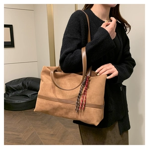 Grand cabas en velours marron avec anses en cuir et détail pompon porté par un mannequin
