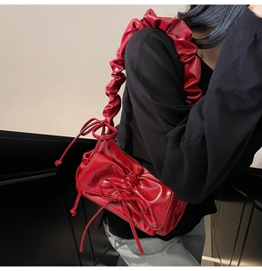 Detail view of red glossy patent leather shoulder bag with ruffled bow strap on model