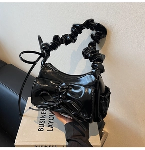 Detail of glossy black bow handbag showing pleated handle and shiny patent texture