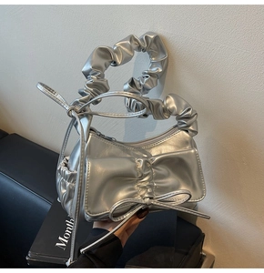 Detailed close-up of a silver metallic pleated handbag with a large decorative bow tie