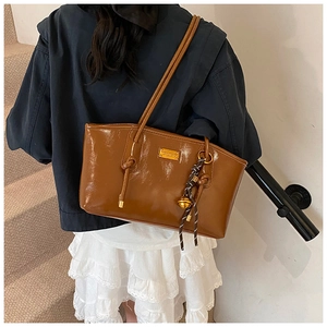 Detail of a brown glossy tote bag with gold metal plaque and woven bell charm accessory