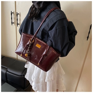 Detail of burgundy glossy leather tote bag with gold logo plaque and braided charm