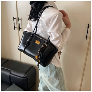 Macro view of black glossy shoulder bag with golden metal plaque and woven charm detail