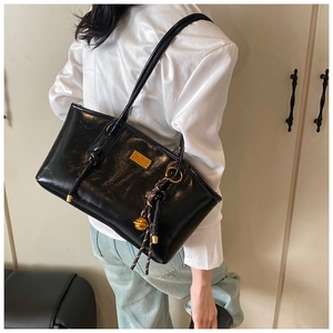 Detail of glossy black patent leather tote bag with gold metal plate and woven pendant