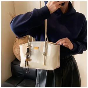Close-up of cream shoulder bag with golden metallic nameplate and woven ball charm
