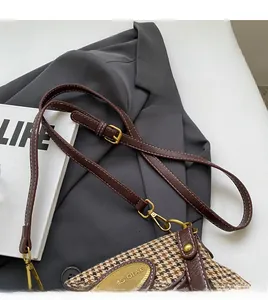 Detail of retro houndstooth bag showing adjustable brown leather shoulder strap with gold hardware