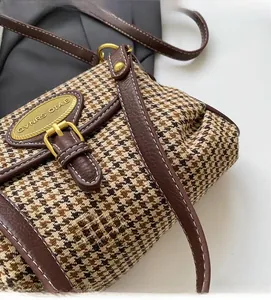 Detail of vintage houndstooth fabric with brown leather trim and golden metal logo plate
