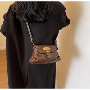 Detail view of deep brown vintage crossbody bag with pleated leather and gold logo plaque